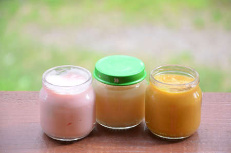 Three jars of baby food on the background of foliage. Pink light yellow orange colorの写真素材