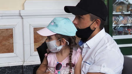 Father with daughter in his arms, son sits wearing masks at station or at the airport, waiting for the train. Family in face mask. Virus. Coronavirus and flu pandemic. Safe travel with child and babyの写真素材