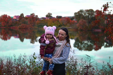 mom and daughter walk by the lake in autumn. Against a background of autumn colours and leaves, a mother smiling next to her daughter. The trees are reflected in the lake.の写真素材