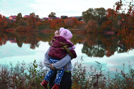 mom and daughter walk by the lake in autumn. Against a background of autumn colours and leaves, a mother smiling next to her daughter. The trees are reflected in the lake.の写真素材