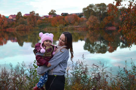 mom and daughter walk by the lake in autumn. Against a background of autumn colours and leaves, a mother smiling next to her daughter. The trees are reflected in the lake.の写真素材
