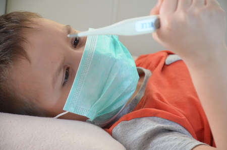 Sick Teenager with Thermometer in the Bed. fever, virus. waiting for a doctor. is treated at home. mom treats sonの写真素材