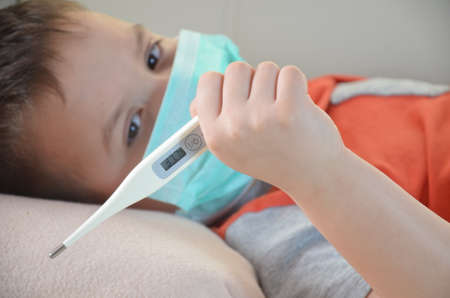 Sick Teenager with Thermometer in the Bed. fever, virus. waiting for a doctor. is treated at home. mom treats sonの写真素材