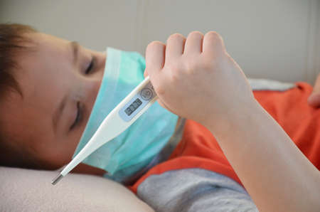 Sick Teenager with Thermometer in the Bed. fever, virus. waiting for a doctor. is treated at home. mom treats sonの写真素材