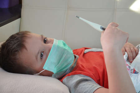 Sick Teenager with Thermometer in the Bed. fever, virus. waiting for a doctor. is treated at home. mom treats sonの写真素材