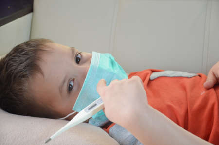 Sick Teenager with Thermometer in the Bed. fever, virus. waiting for a doctor. is treated at home. mom treats sonの写真素材
