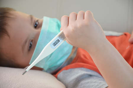 Sick Teenager with Thermometer in the Bed. fever, virus. waiting for a doctor. is treated at home. mom treats sonの写真素材