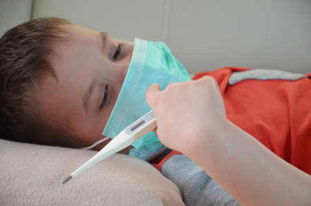 Sick Teenager with Thermometer in the Bed. fever, virus. waiting for a doctor. is treated at home. mom treats sonの写真素材