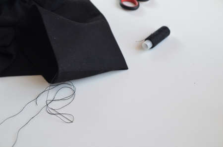 girl sews with thread and needle black material. hemming trousers. twists the thread into a needle. Tailor man working in his tailor shop, Tailoring, close upの写真素材