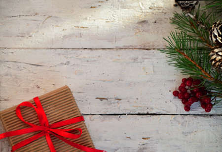 Christmas gift box with decoration. box tied with a red ribbon, a branch of a Christmas tree with cones, top view, flat lay, on a white wooden backgroundの写真素材