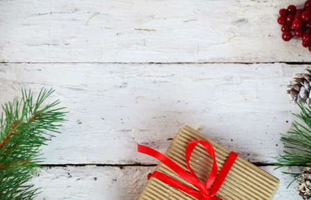 Christmas or new year gift box with decoration. box tied with a red ribbon, a branch of a Christmas tree with cones, top view, flat lay, on a white wooden backgroundの写真素材