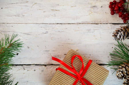 Christmas or new year gift box with decoration. box tied with a red ribbon, a branch of a Christmas tree with cones, top view, flat lay, on a white wooden backgroundの写真素材