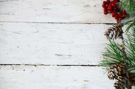 Merry Christmas and Happy New Year a branch of a Christmas tree with cones in the snow on a white wooden background with red berries then view flat lay copy spaceの写真素材