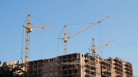 Working on place with many tall buildings under construction and cranes under a blue skyの写真素材