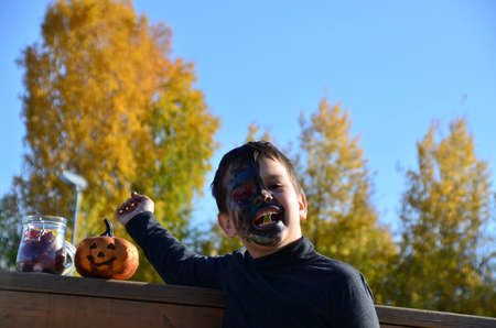 boy with black makeup for halloween, zombie. Scary little boy smiling wearing skull makeup for halloween halloween pumpkin lantern, sweetsの写真素材