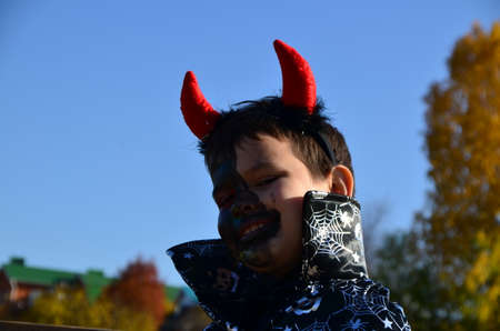 funny baby in devil halloween costume with horns and trident on a dark wooden background boy with black makeup for halloween, zombieの写真素材