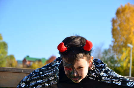 funny baby in devil halloween costume with horns and trident on a dark wooden background boy with black makeup for halloween, zombieの写真素材