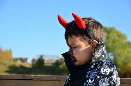 funny baby in devil halloween costume with horns and trident on a dark wooden background boy with black makeup for halloween, zombieの写真素材