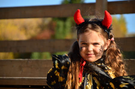 little cute girl in the image devil on Halloween. red horns on the head with black grimm for halloween zombieの写真素材