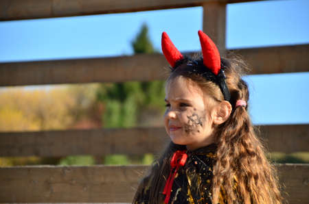 little cute girl in the image devil on Halloween. red horns on the head with black grimm for halloween zombieの写真素材