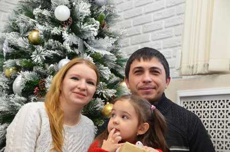 lovely family on a winter evening, enjoying the warm Christmas atmosphere in their living room near an elegant Christmas tree, mother father and child wearing wait of Santa Claus. New yearの写真素材