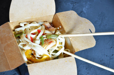 Asian food and chopsticks on wooden table. takeout boxes with noodles with chicken meat and rice with seafood cocktail and vegetables. Fast food delivery.の写真素材