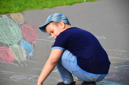 Child drawing sun and house on asphalt in a park on the playground or sidewalk, happy childhood, summer vacation, entertainment for childrenの写真素材