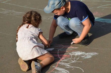 Child drawing sun and house on asphalt in a park on the playground or sidewalk, happy childhood, summer vacation, entertainment for childrenの写真素材