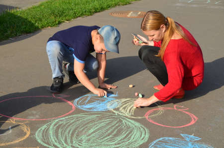 Child drawing sun and house on asphalt in a park on the playground or sidewalk, happy childhood, summer vacation, entertainment for childrenの写真素材