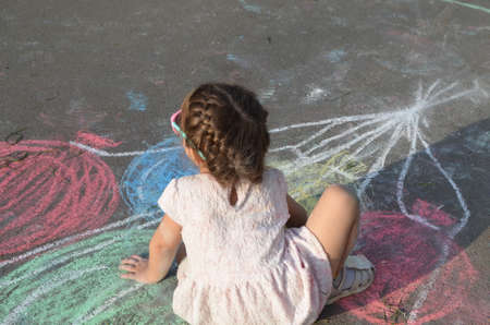 Child drawing sun and house on asphalt in a park on the playground or sidewalk, happy childhood, summer vacation, entertainment for childrenの写真素材