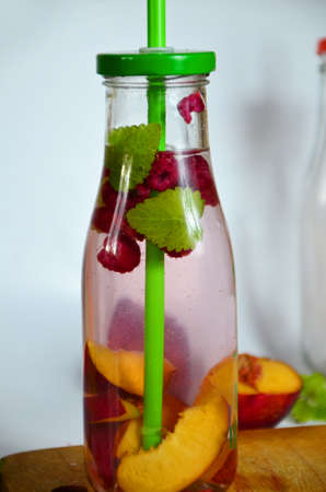 Healthy detox fruit infused flavored water. Summer refreshing homemade cocktail with fruits and thyme on white in a bottle on a white background.の写真素材