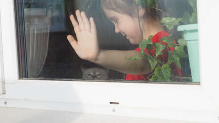 Beautiful little girl smiling and watching out the window. A child looks out the window. Portrait of...