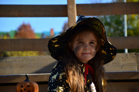 a girl in a witch suit and a black hat on the head with black Halloween make-up, zombie eating sweets jelly worms at a celebration of Halloweenの写真素材