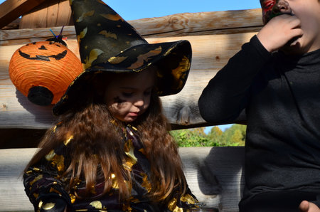 children in halloween costumes on holiday a girl in a witch suit a black hat on the head with black Halloween make-up, boy in devil halloween costume with horns zombie eating sweets jelly wormsの写真素材