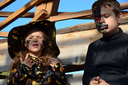 children in halloween costumes on holiday a girl in a witch suit a black hat on the head with black Halloween make-up, boy in devil halloween costume with horns zombie eating sweets jelly wormsの写真素材