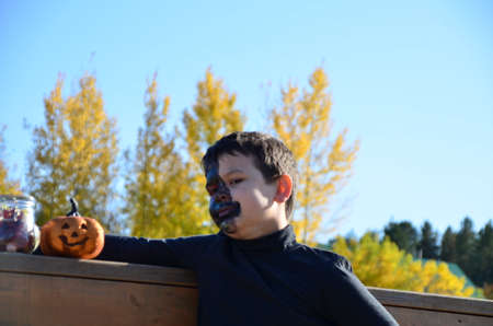 boy with black makeup for halloween, zombie. Scary little boy smiling wearing skull makeup for halloween halloween pumpkin lantern, sweetsの写真素材