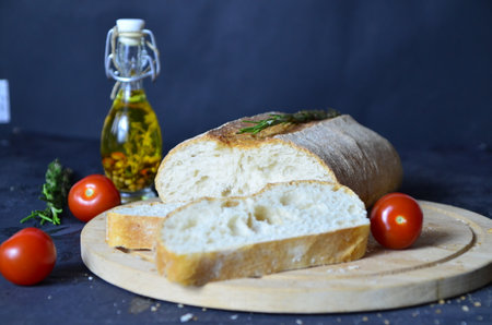 Italian ciabatta bread cut in slices on wooden chopping board with herbs, garlic and olives over...
