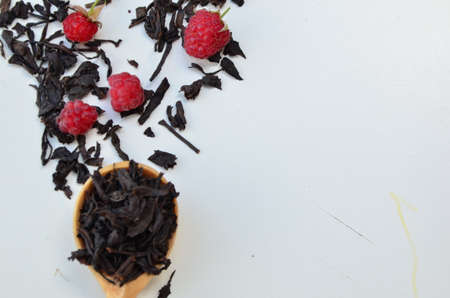 dry black tea in a wooden spoon on a white plate with raspberries and mint. healthy healing berry teaの写真素材