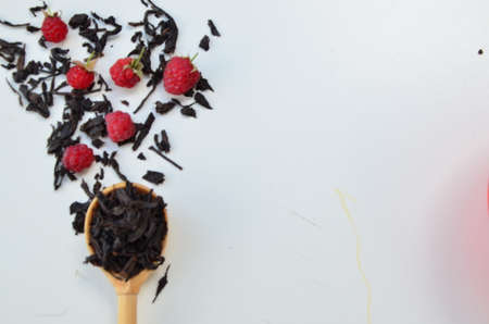 dry black tea in a wooden spoon on a white plate with raspberries and mint. healthy healing berry teaの写真素材
