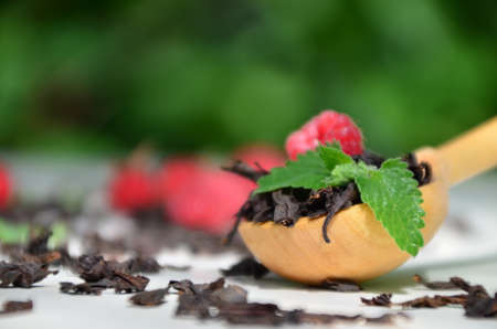 dry black tea in a wooden spoon on a white plate with raspberries and mint. healthy healing berry teaの写真素材