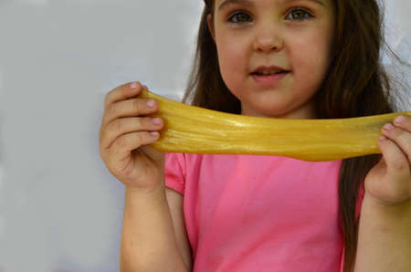 Cute funny playing girl with colorful slime isolated on white background. Little girl stretching yellow slime to the sides. Kids hands playing slime toy. Making slime.の写真素材