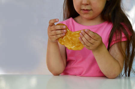 Cute funny playing girl with colorful slime isolated on white background. Little girl stretching yellow slime to the sides. Kids hands playing slime toy. Making slime.の写真素材