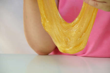 Cute funny playing girl with colorful slime isolated on white background. Little girl stretching yellow slime to the sides. Kids hands playing slime toy. Making slime.の写真素材