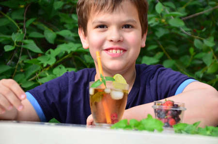 Child boy drinks natural lemonade summer drink, tea with wild berries, lime, raspberries and blueberries, summer vacation in park. refreshing natural drink lemonade Detox fruit infused water cocktailの写真素材