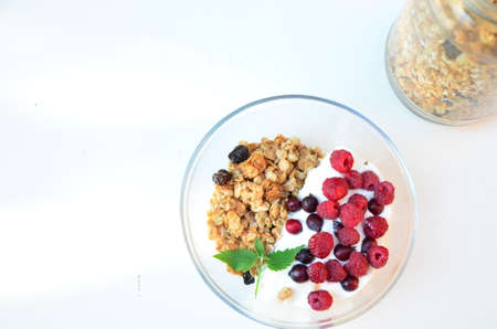 Healthy breakfast bowl with homemade granola. proper nutrition bowl of oat granola with yogurt, fresh raspberries, blueberries, strawberries, blackberries nuts with spoon on white for healthy food.の写真素材