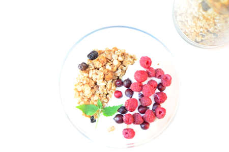Healthy breakfast bowl with homemade granola. proper nutrition bowl of oat granola with yogurt, fresh raspberries, blueberries, strawberries, blackberries nuts with spoon on white for healthy food.の写真素材