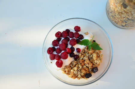 Healthy breakfast bowl with homemade granola. proper nutrition bowl of oat granola with yogurt, fresh raspberries, blueberries, strawberries, blackberries nuts with spoon on white for healthy food.の写真素材
