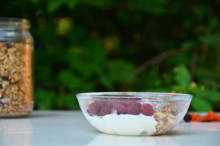 Healthy breakfast bowl with homemade granola. proper nutrition bowl of oat granola with yogurt, fresh raspberries, blueberries, strawberries, blackberries nuts with spoon on white for healthy food.の写真素材