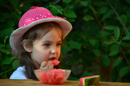 Funny portrait of an incredibly beautiful little girl eating watermelon, healthy fruit snack, adorable toddler child with curly hair playing in a sunny garden on a hot summer day. portraitの写真素材