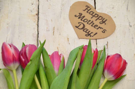 Tulips and a heart with the inscription happy mother day of Mom and gifts on a white wooden background.の写真素材